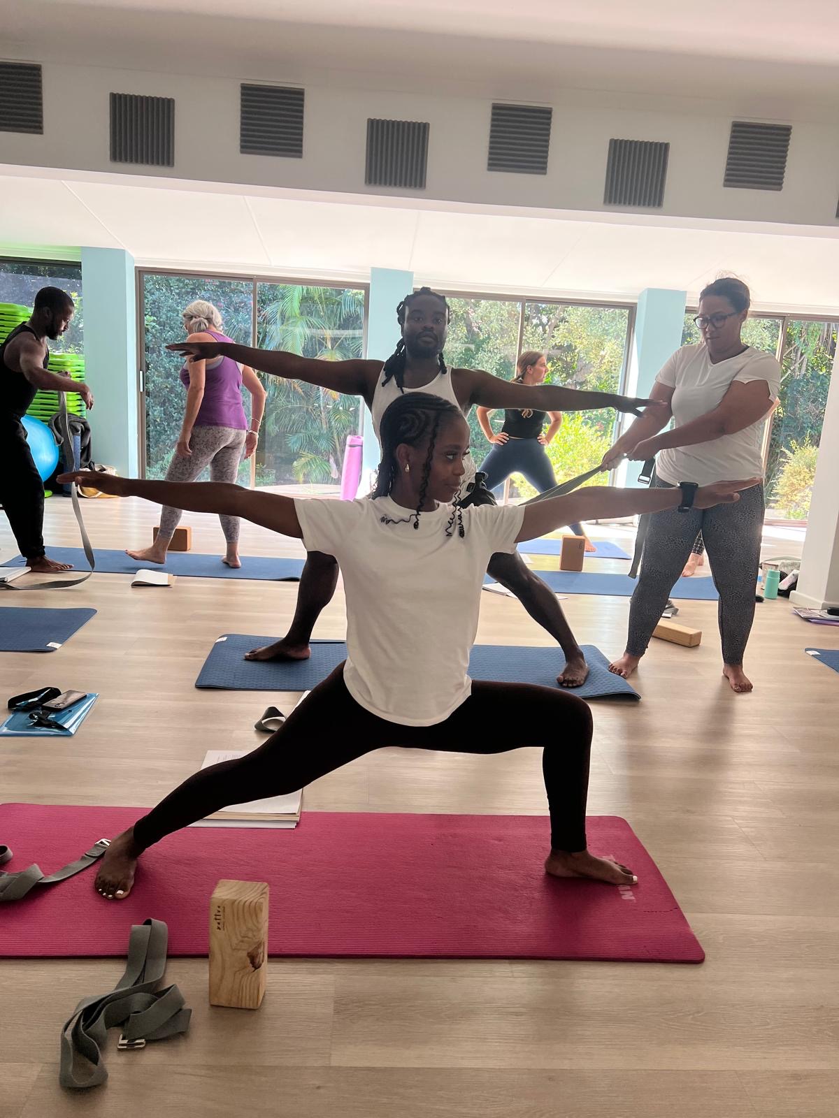 Trainee learning Warrior II alignment with a yoga strap assist